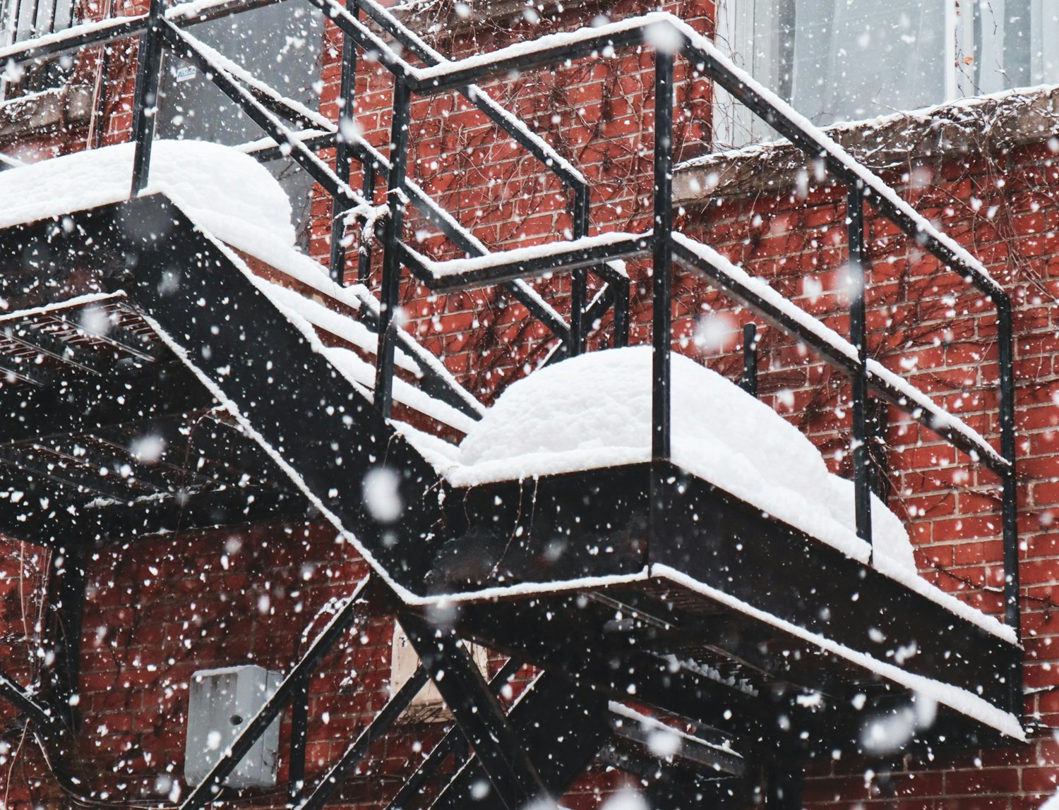 Snow-covered exterior metal stairs and handrails against a brick building
